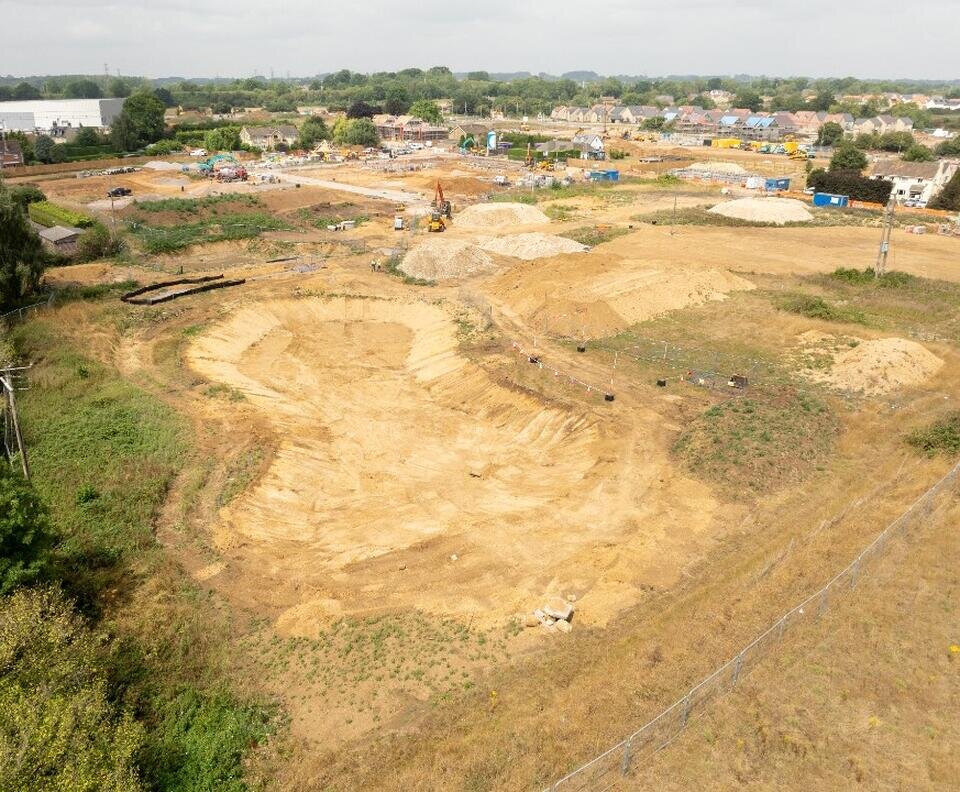A wide shot of a large section of earth that has been levelled off. In the background are cranes.