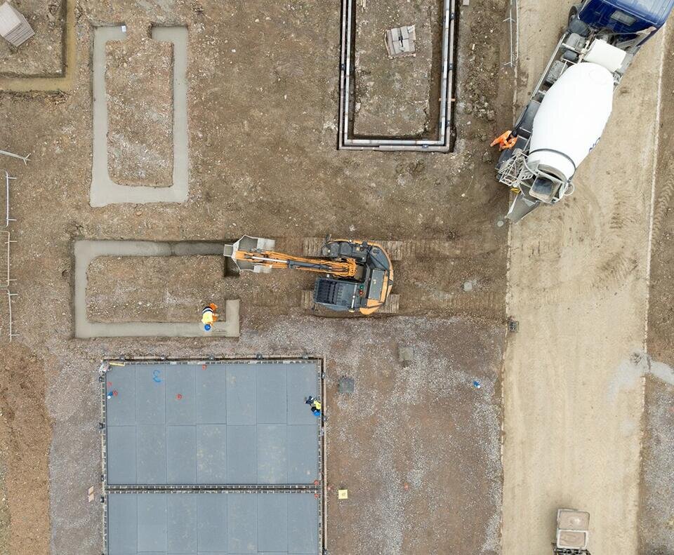 A drone image of a digger and cement mixer pouring concrete foundations