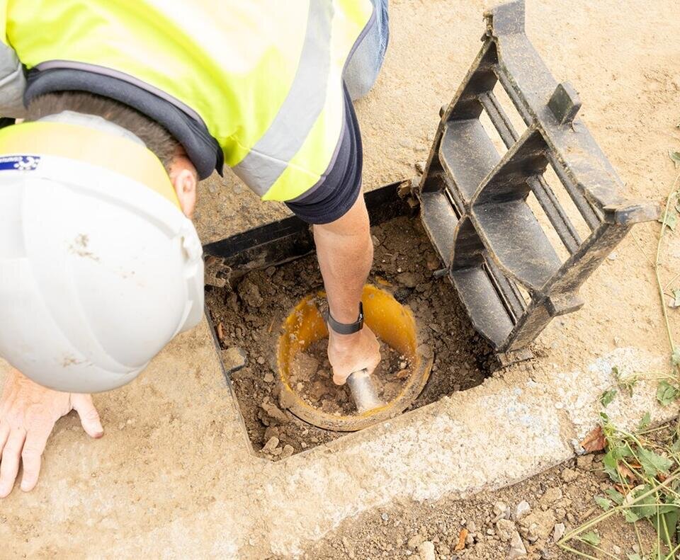A groundworker reaches into a hole in thr ground to reach burried utilities