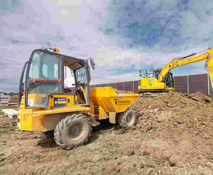 A yellow dumper with a safety shield pours muck onto a pile of earth while a yellow digger spreads the muck