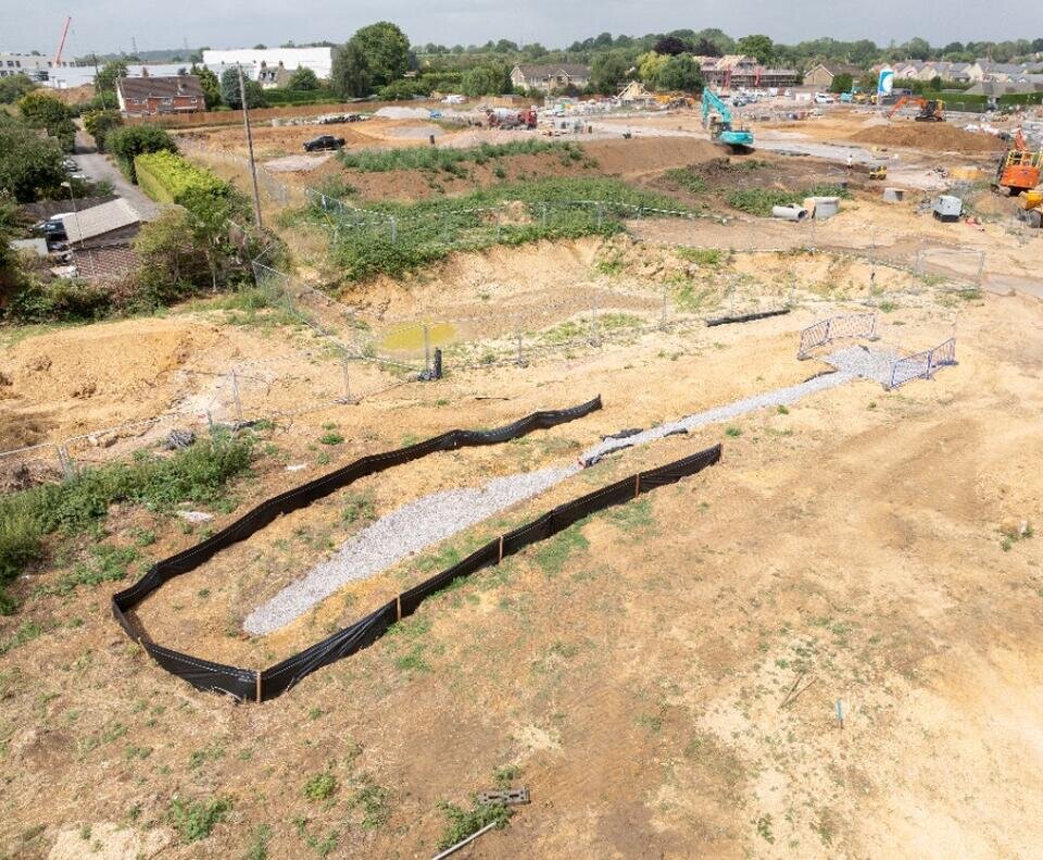 A plot of land with diggers in the background. The ground has some concrete poured into it but mainly is mud.