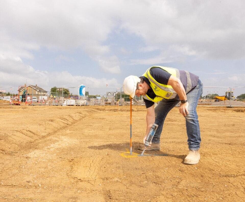 a groundsworker in a high vis and white hard hat using spray paint on earth